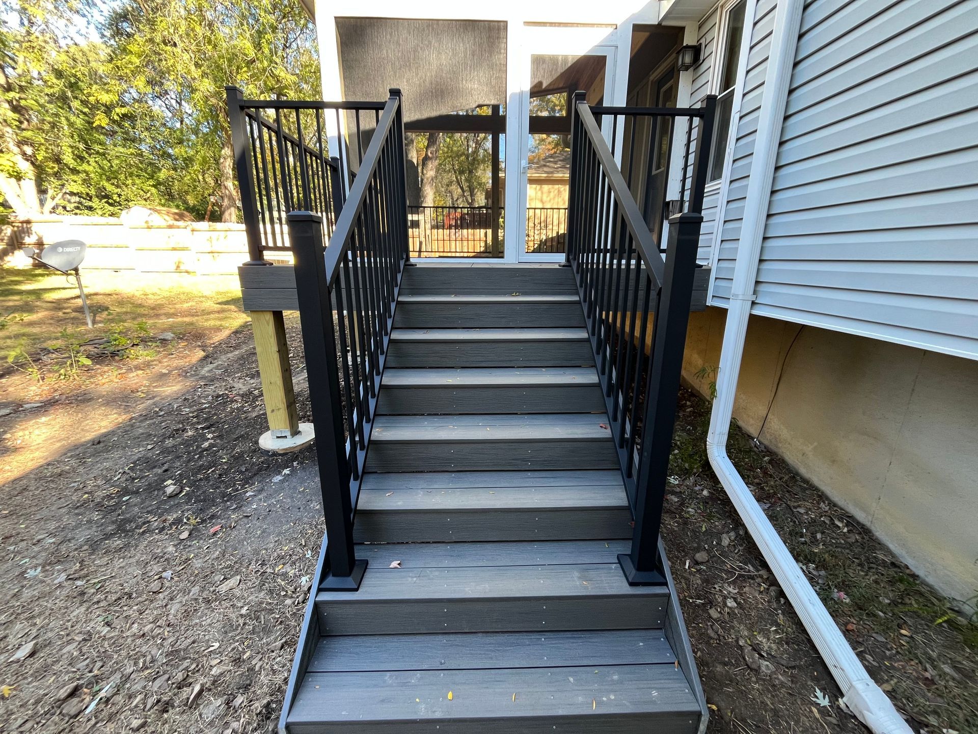 Stairs leading up to a screened-in porch with black railings, built on a gray composite deck, next to a house.