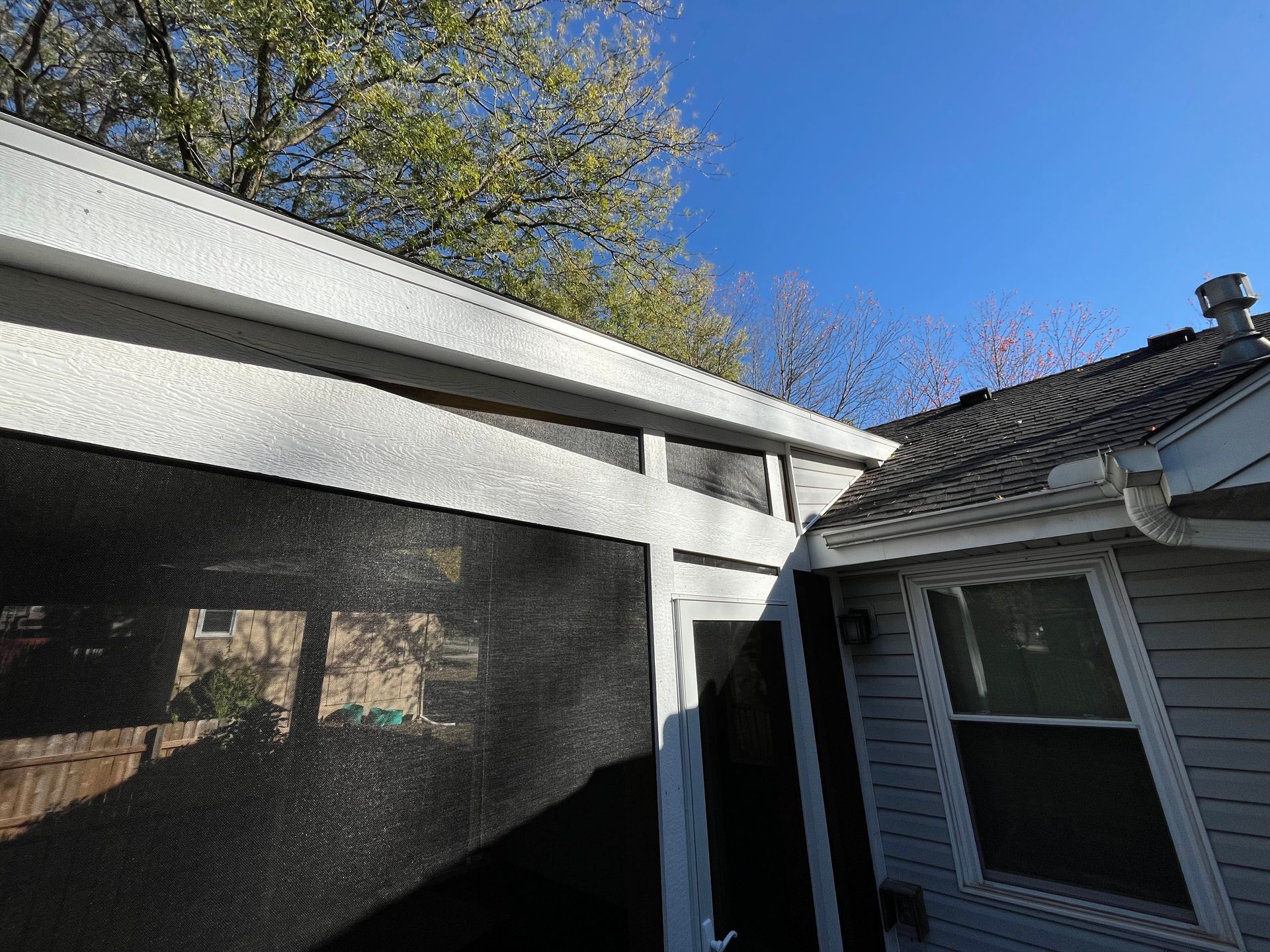Exterior view of a screened porch, white siding, and part of a house with a dark roof on a sunny day.