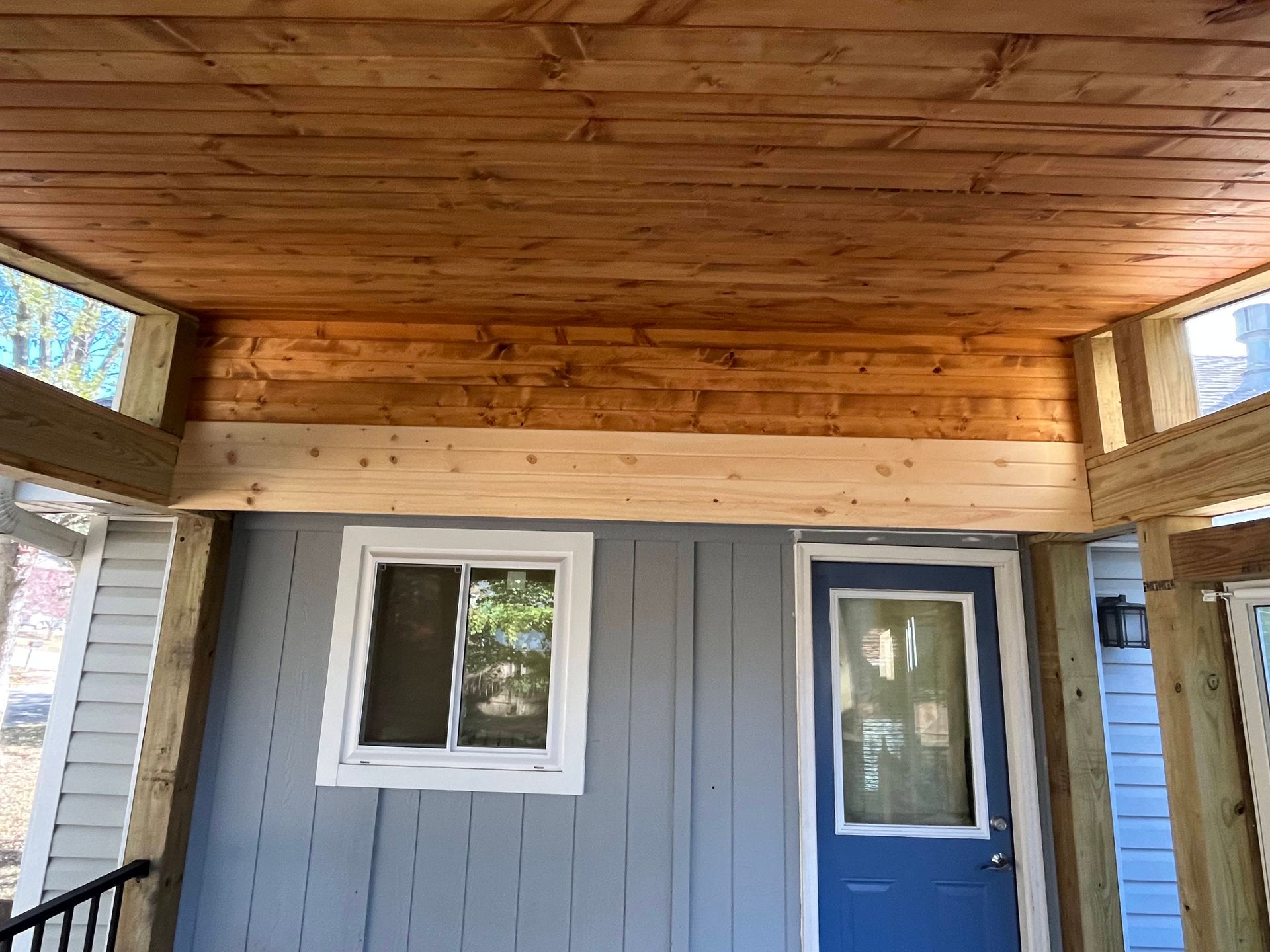 Wooden porch ceiling and beams. Blue door and window against gray siding.
