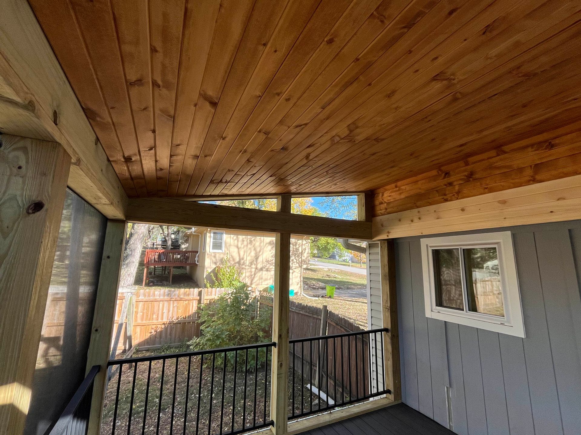 Wooden porch with ceiling, railing, and view of yard.