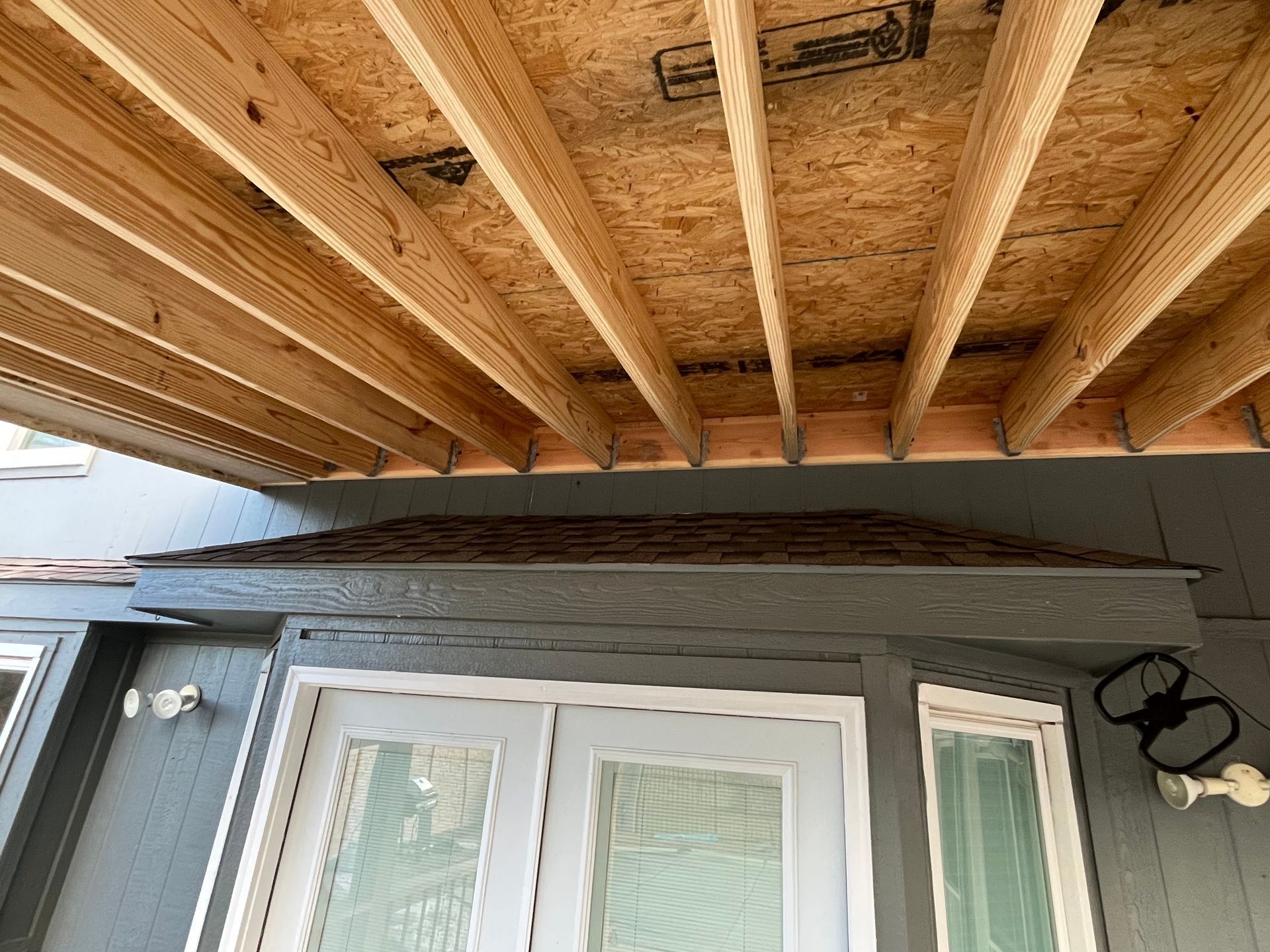 Low-angle view of a wooden deck ceiling above a gray house exterior with a door and window.