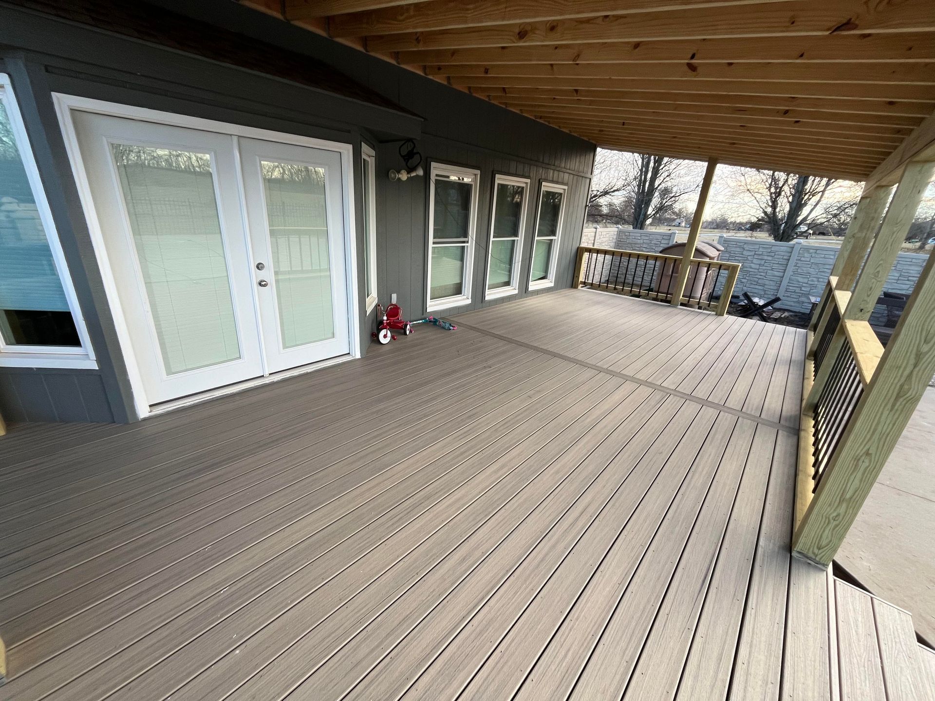 Wooden deck with a covered porch. White doors and windows on a gray house.