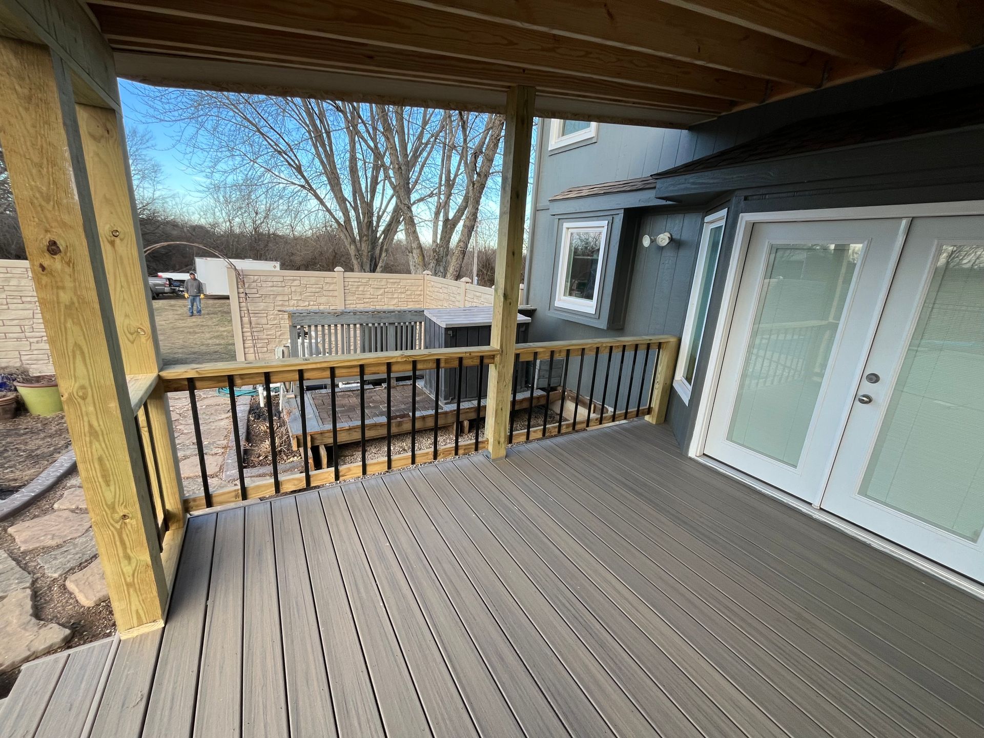 Wooden deck with gray planks and black railing, overlooking a yard and house.