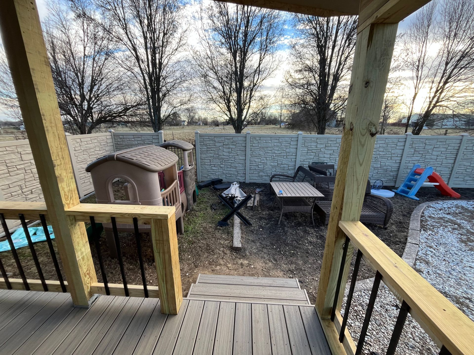 Wooden deck with stairs leads to backyard with playhouse, fence, and trees.