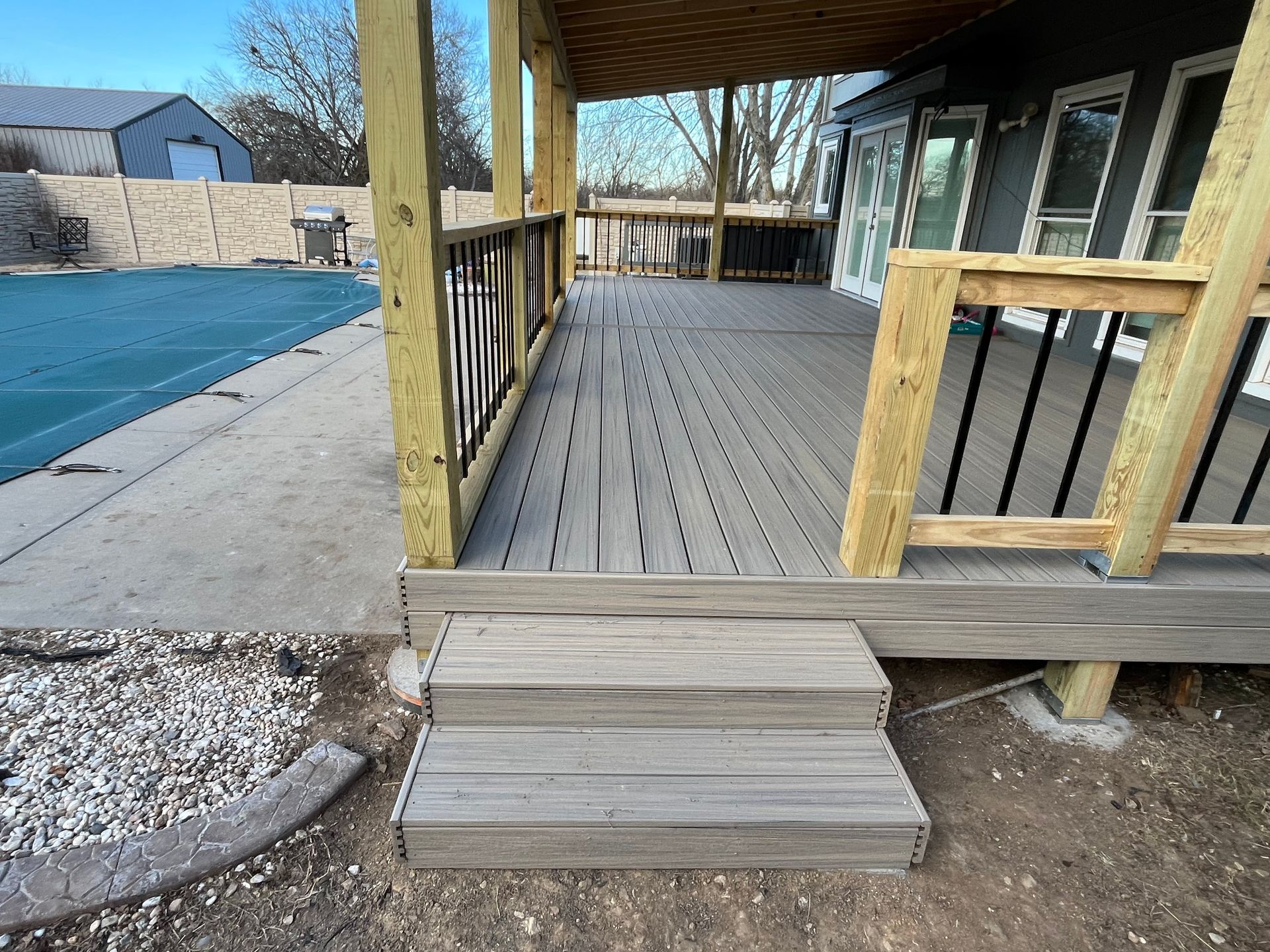 A wooden deck with steps next to a pool. Deck has a roof and railing.