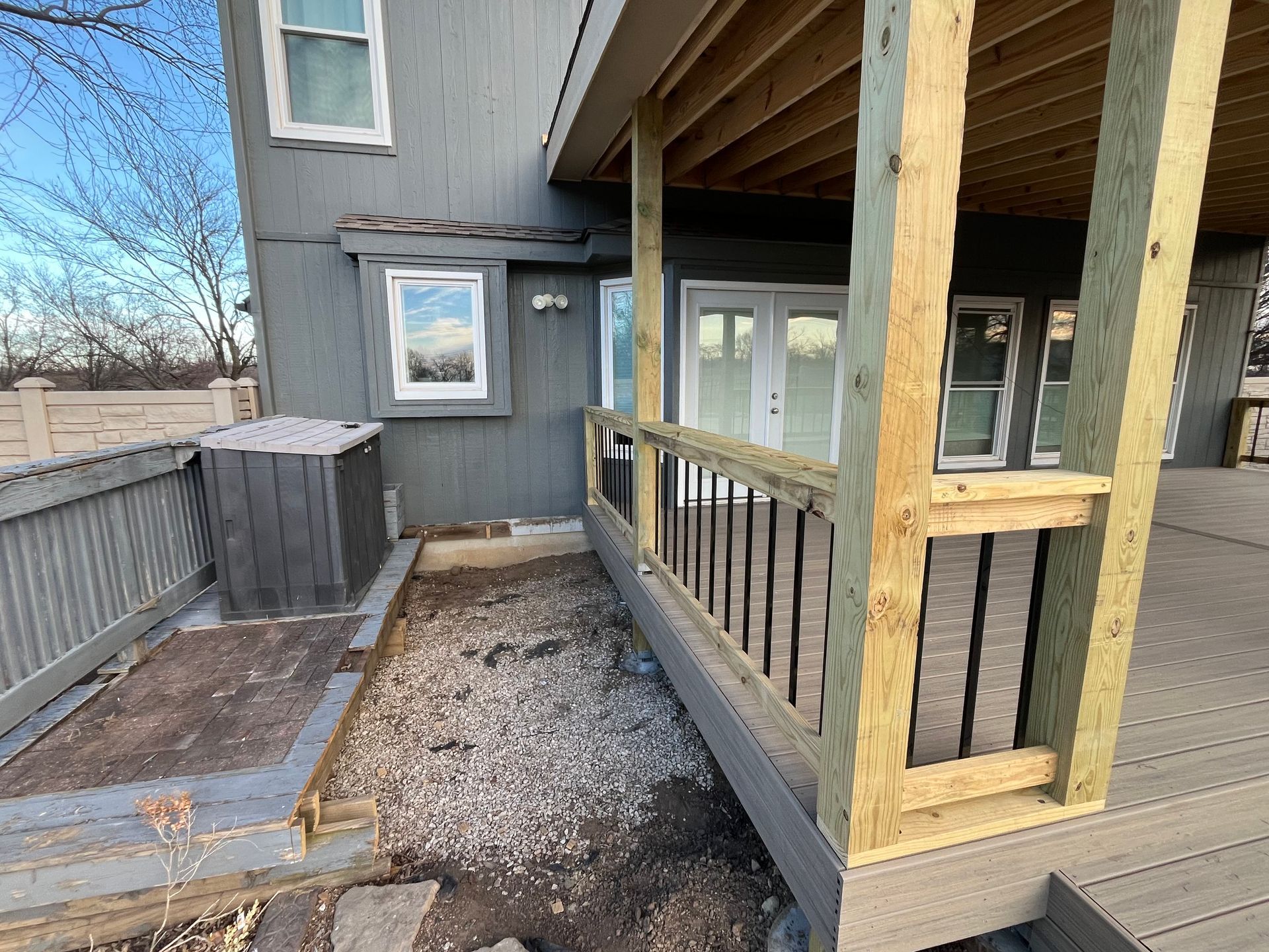 Backyard deck with wooden railing and gravel path leading to house. Gray siding and blue sky.