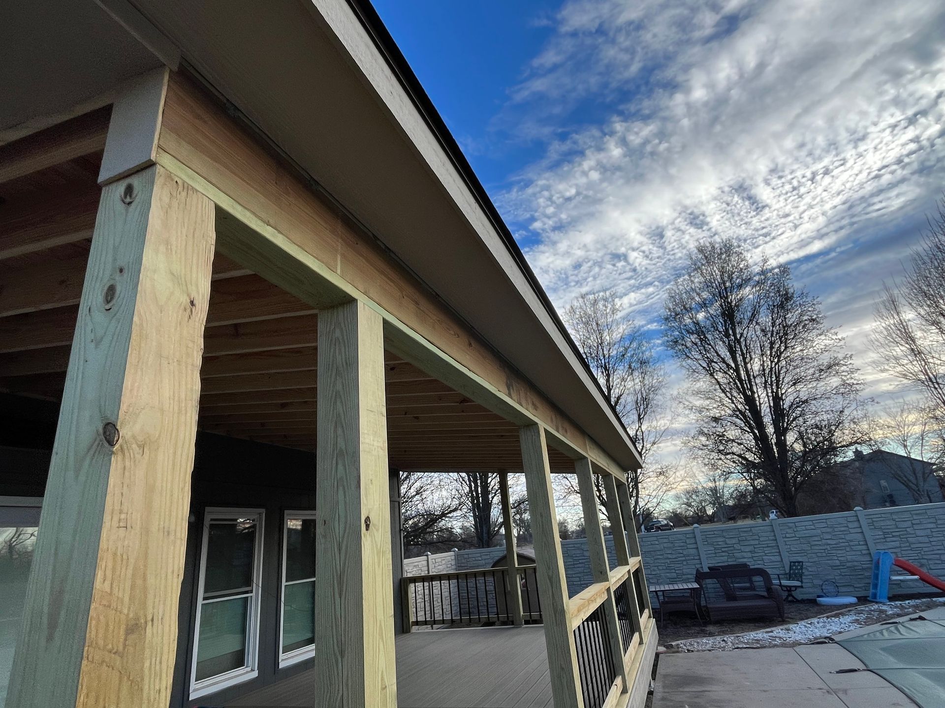 A wooden porch with a roof under a cloudy sky.