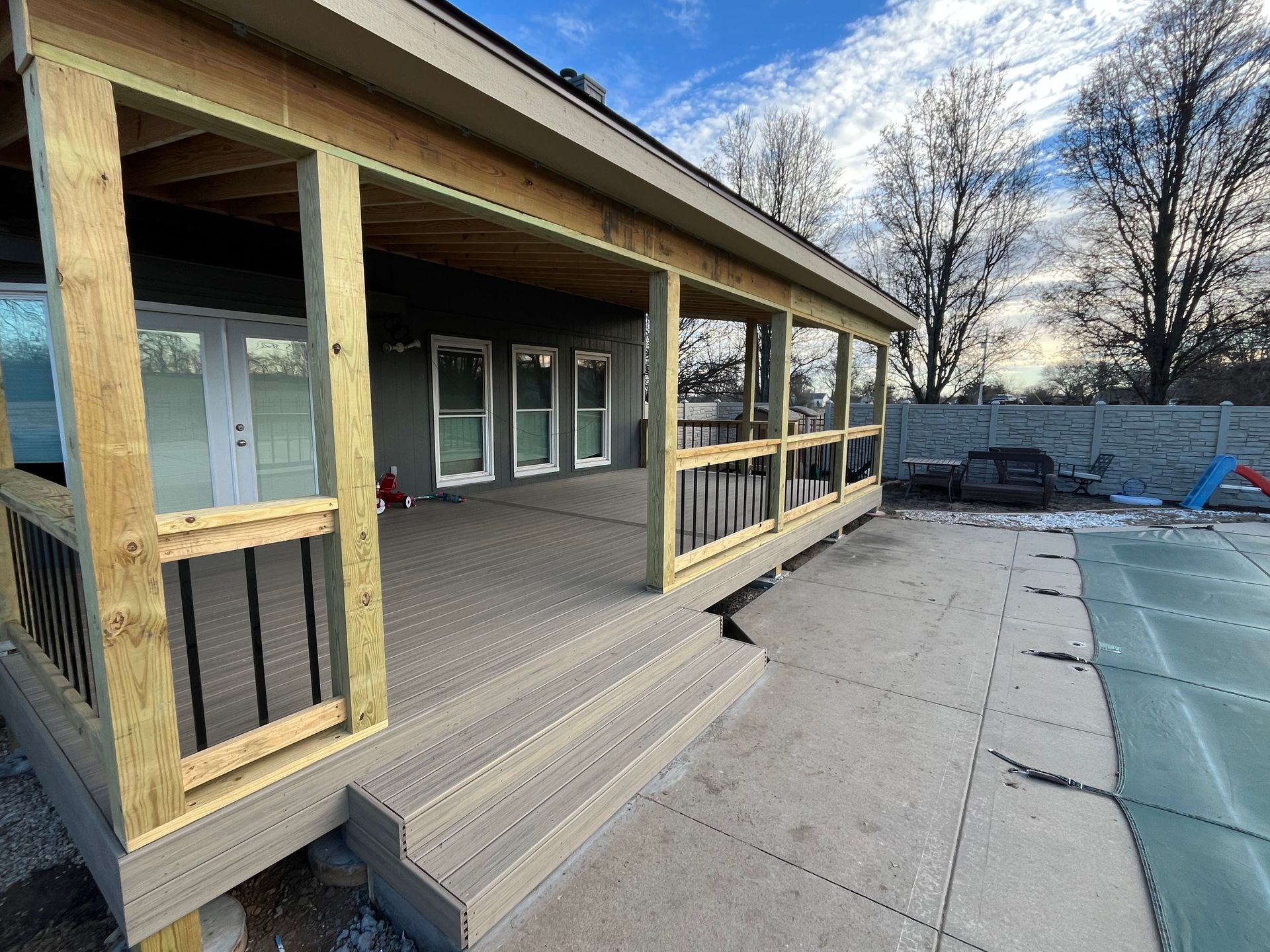 Deck with stairs, partially covered, overlooking a concrete patio and pool.