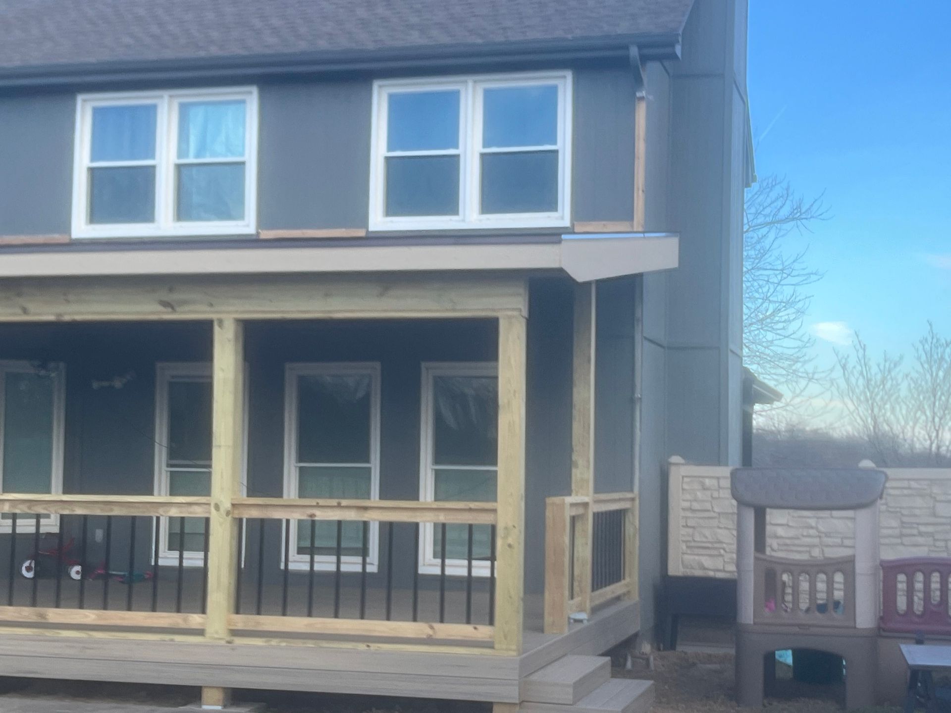 Two-story house with a wooden porch. Gray siding and white-framed windows. Unfinished wood trim.