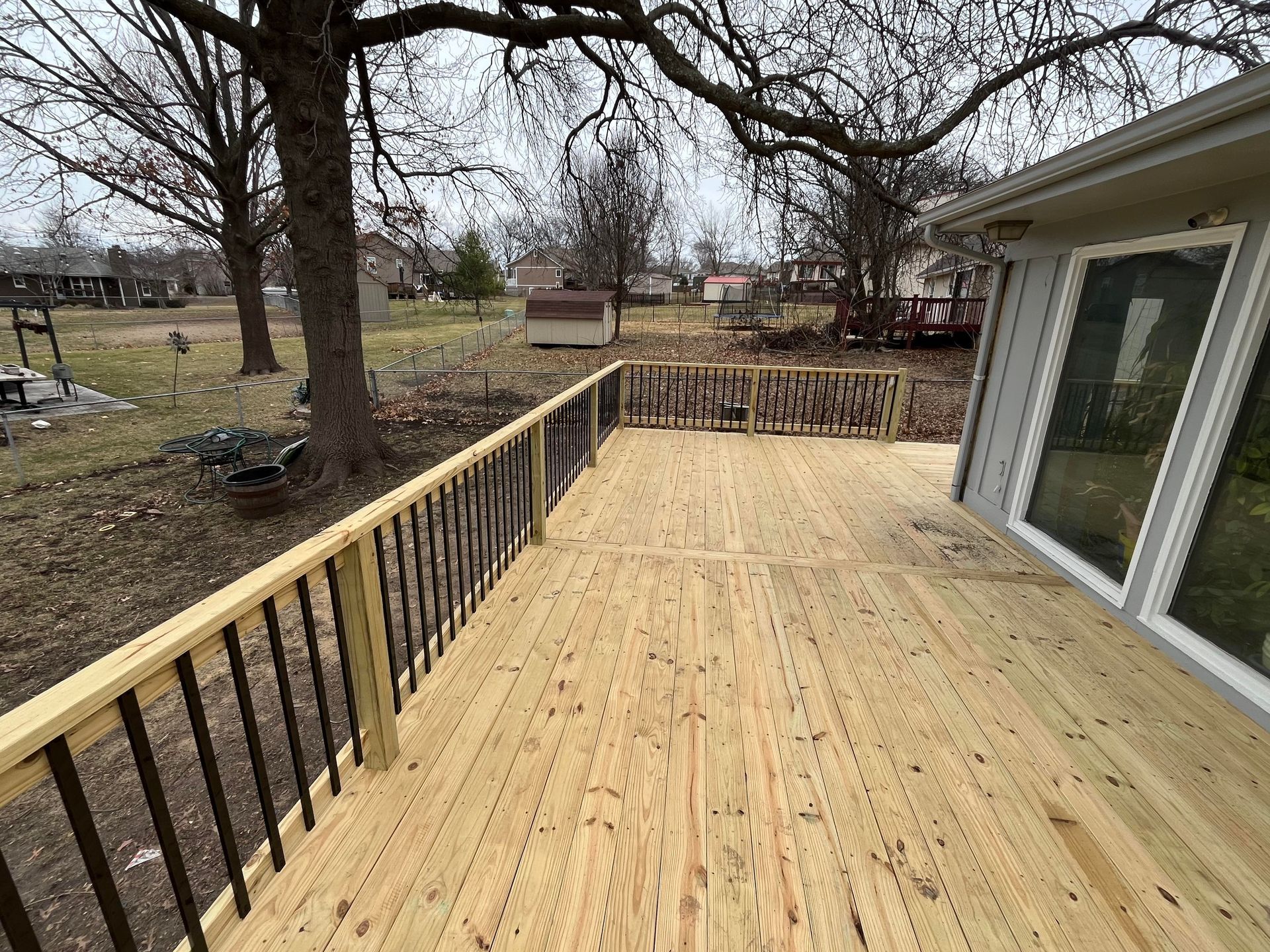 Newly constructed wooden deck with black railing in a backyard setting.