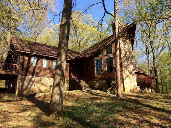 A large log cabin in the middle of a forest surrounded by trees.