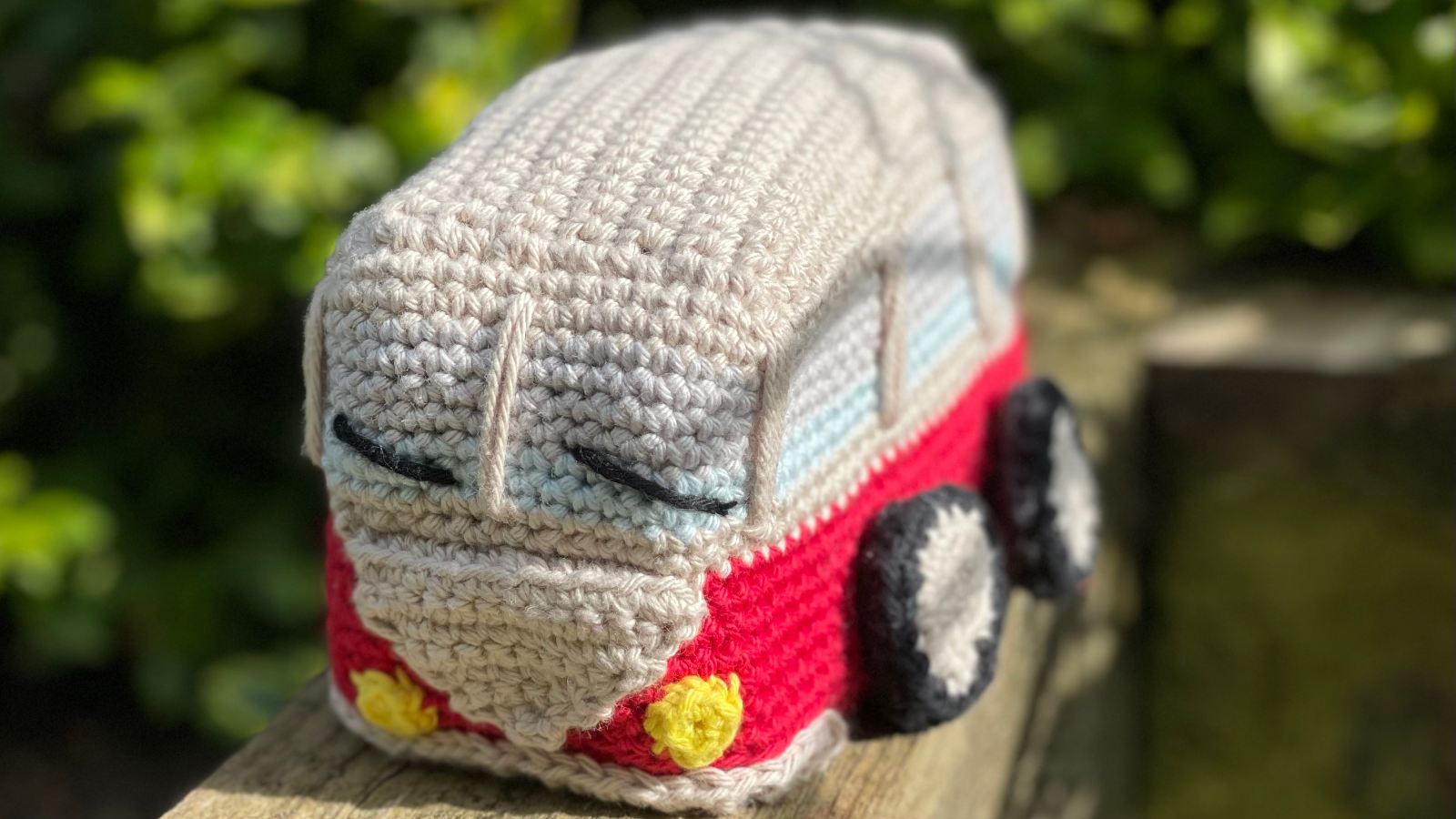 Amigurumi Toy Combi Van. Red body with cream coloured roof, black wheels and yellow lights on the front.