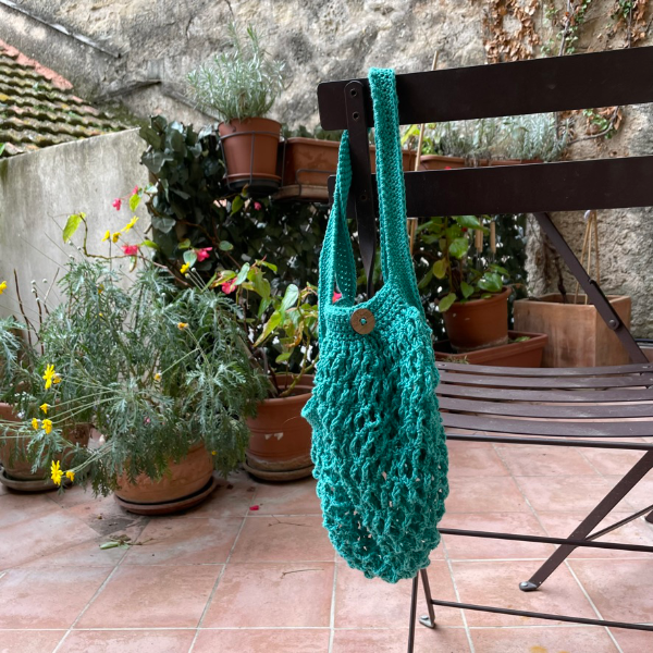 Crochet green string shopping bag hanging over the back of a chair.