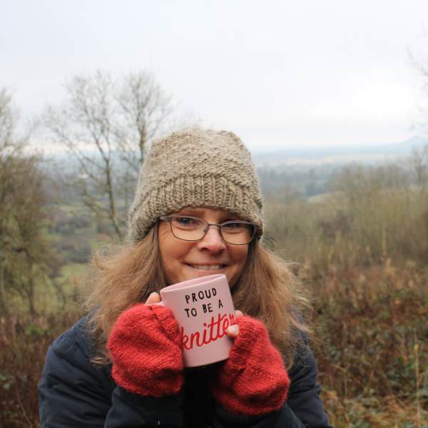 Cathie wearing a grey knitted beanie, holding a mug that says 