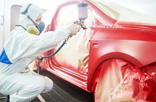 A man is spray painting a red car in a garage.