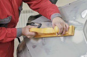 A man is sanding the hood of a car with a sander.