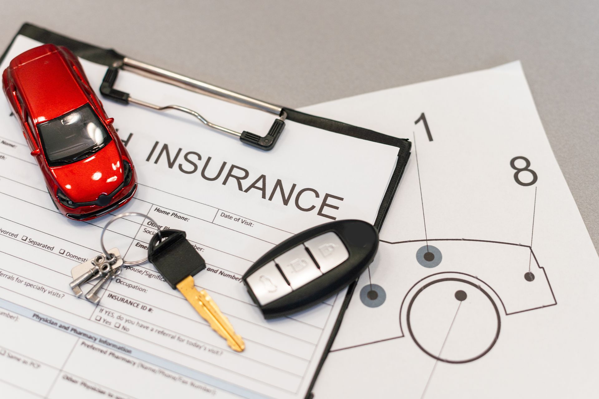 A clipboard with a car , keys and an insurance form on it.