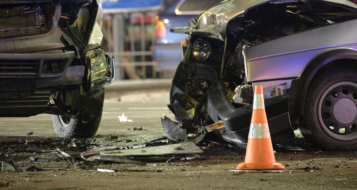 A car accident on a city street with a traffic cone in the foreground.