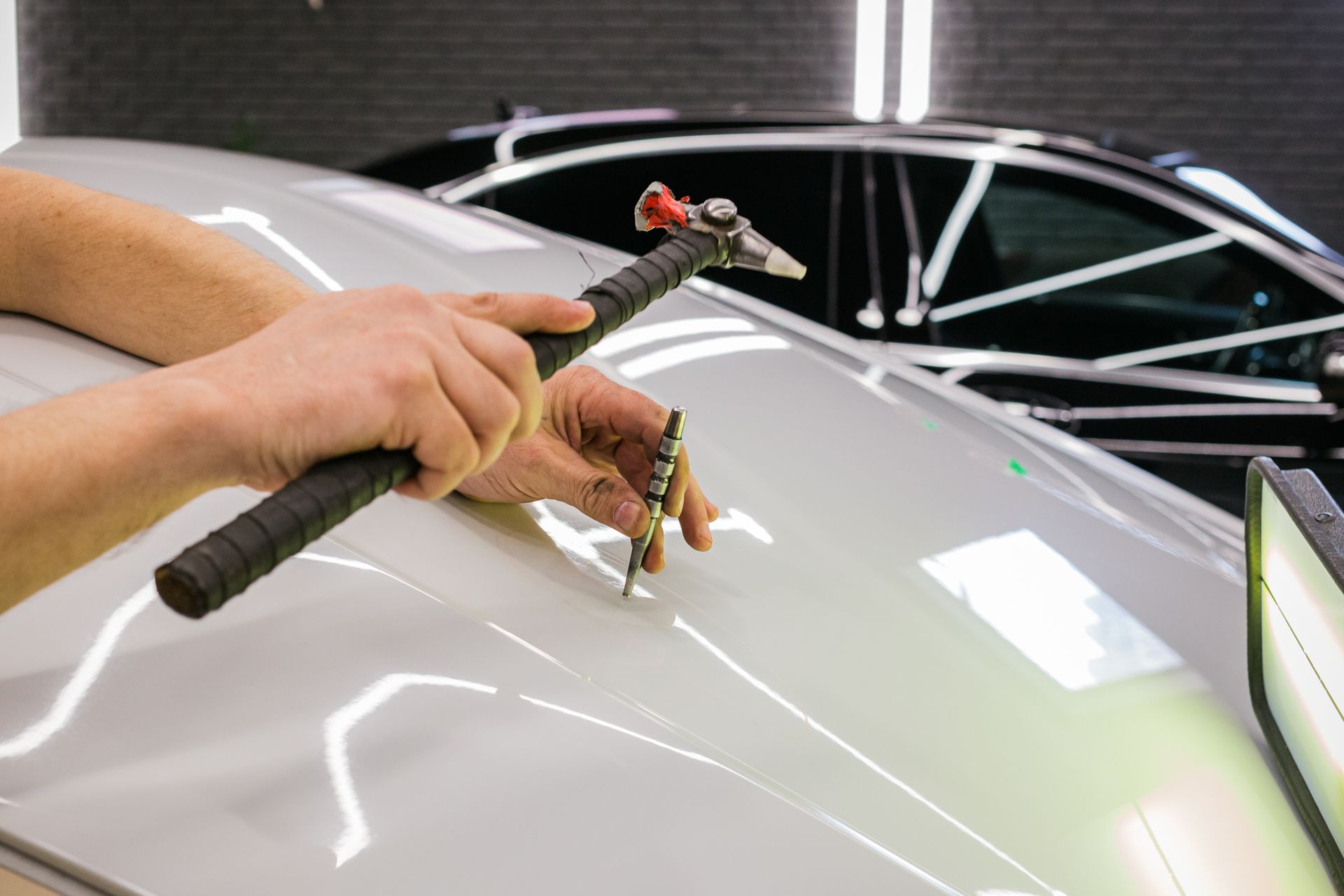 A person is using a hammer to fix a dent on the roof of a car.