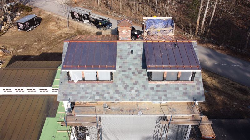 Aerial view of a house roof under construction, showing different roofing materials and a chimney.
