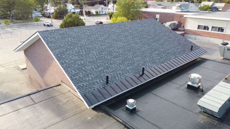 View of a building's roof, showing a sloped asphalt shingle roof above a flat roof.