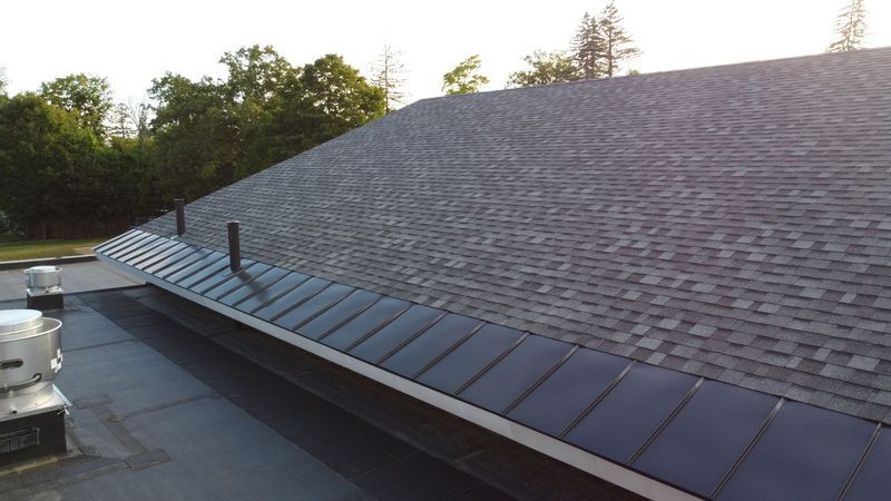 Dark gray shingled roof with a black metal gutter along a flat roof section.