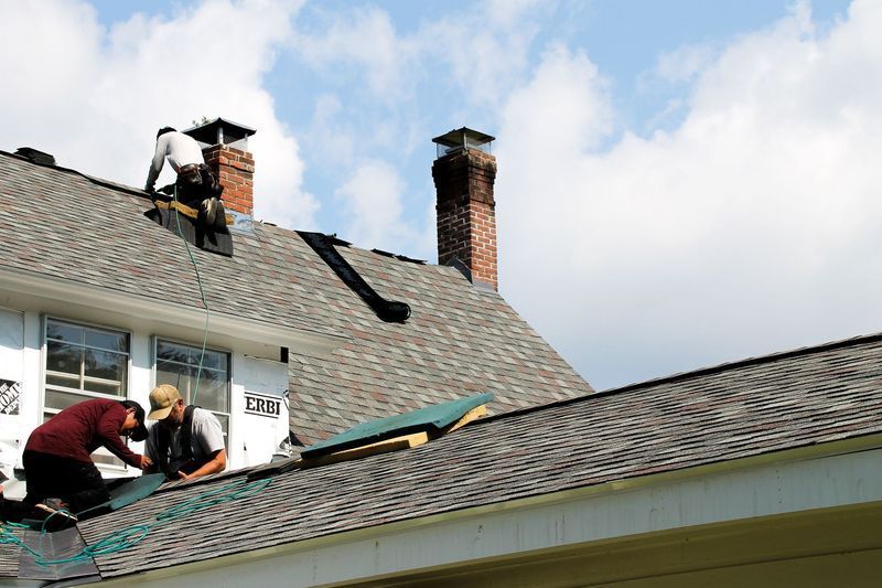 Roofers working on a house roof under a partly cloudy sky. Roofers working on a house roof under a partly cloudy sky.
