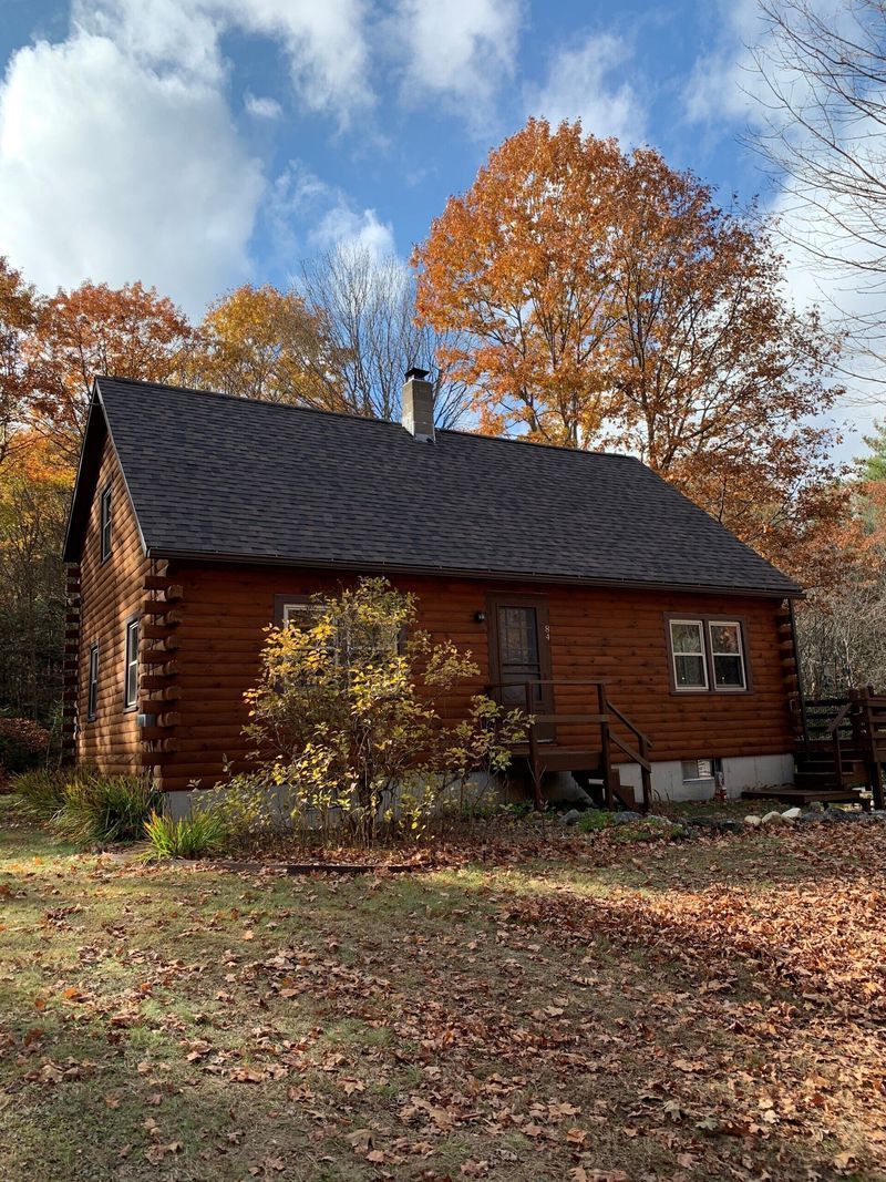 Log cabin with dark roof and autumn foliage.