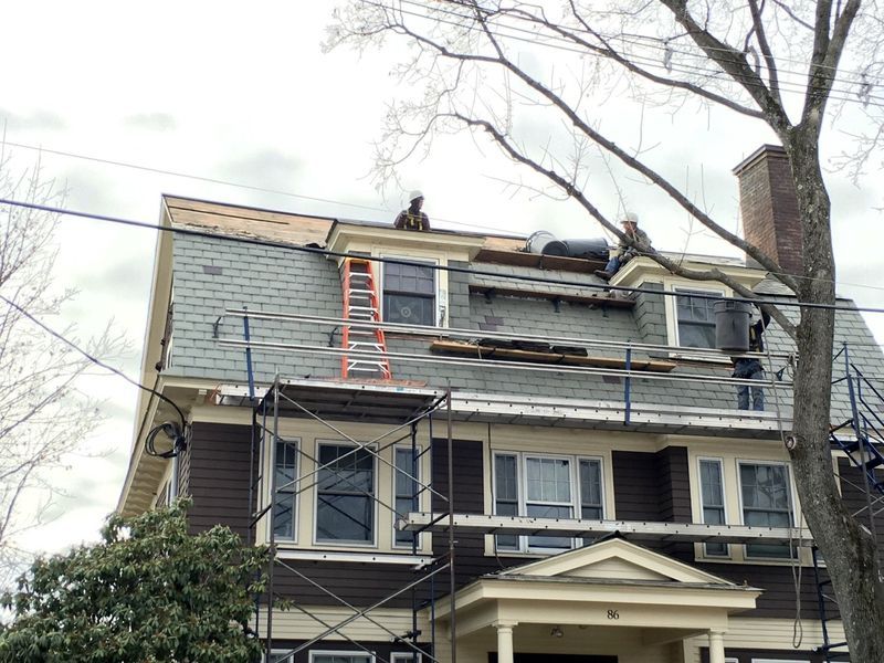 Roofers on a house with a slate roof, repairing shingles. Ladder and scaffolding present. Roofers on a house with a slate roof, repairing shingles. Ladder and scaffolding present.