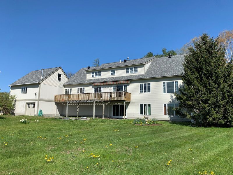 Back of a two-story beige house with a large wooden deck and a detached garage on a grassy lawn under a blue sky.