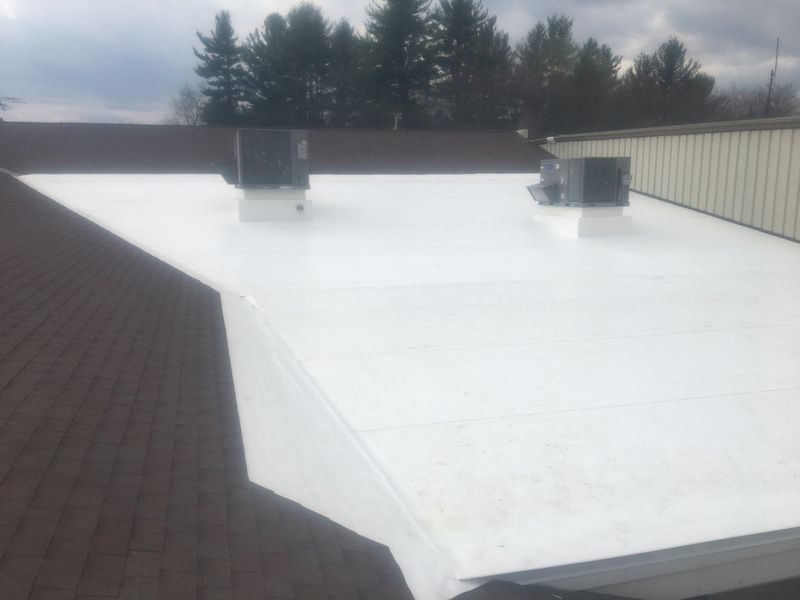 White flat roof on building, brown shingle roof on adjacent building section, AC units.