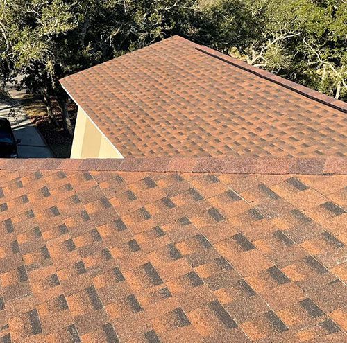 Two adjacent orange-brown shingled roofs viewed from above, with trees in the background