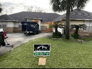 House with moving truck in driveway and lawn sign in front under cloudy sky