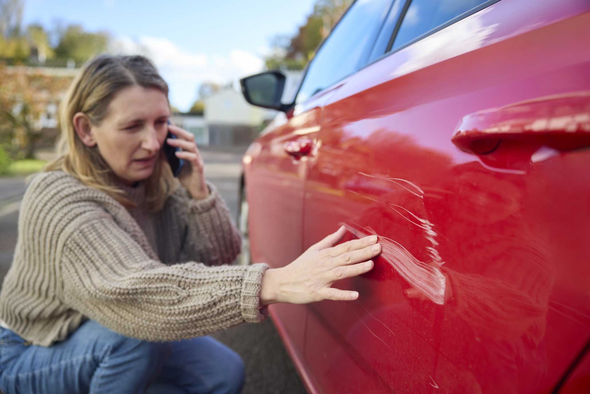 A woman is talking on a cell phone next to a red car.