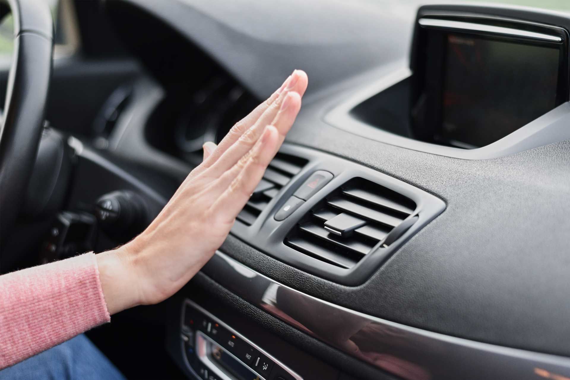 A woman is sitting in a car with her hand on the air vent.