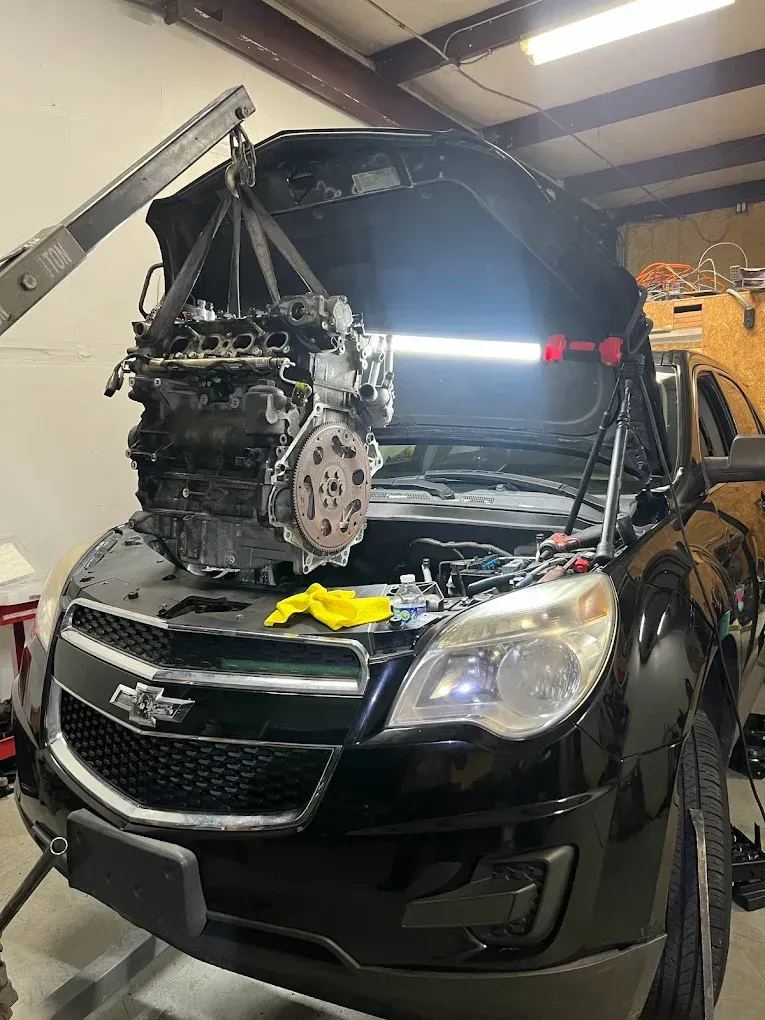 Engine being lifted out of a black Chevy Equinox in a garage with open hood.