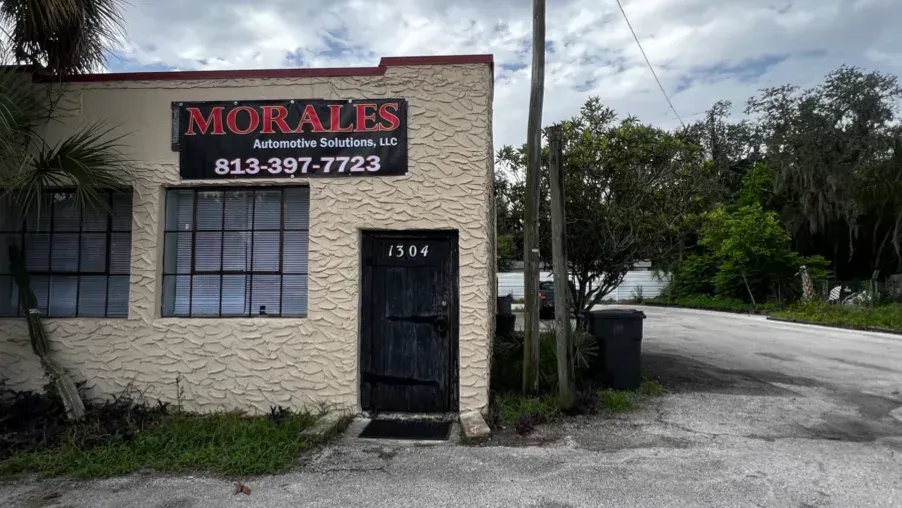 Morales Automotive Solutions storefront. Beige building with black door and windows, sign with phone number.