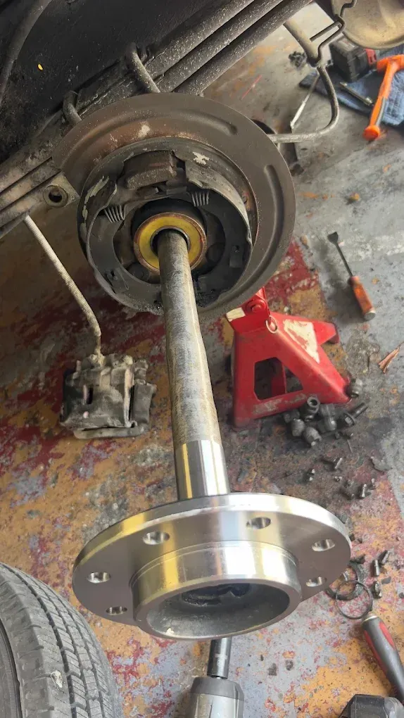 Car axle repair with exposed brake assembly and hub. Silver metal parts against a dirty garage floor.