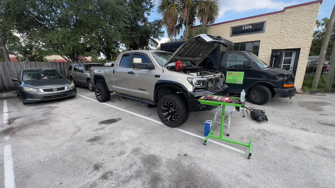Cars parked in a lot; a truck with its hood open, tools and equipment set up beside it.