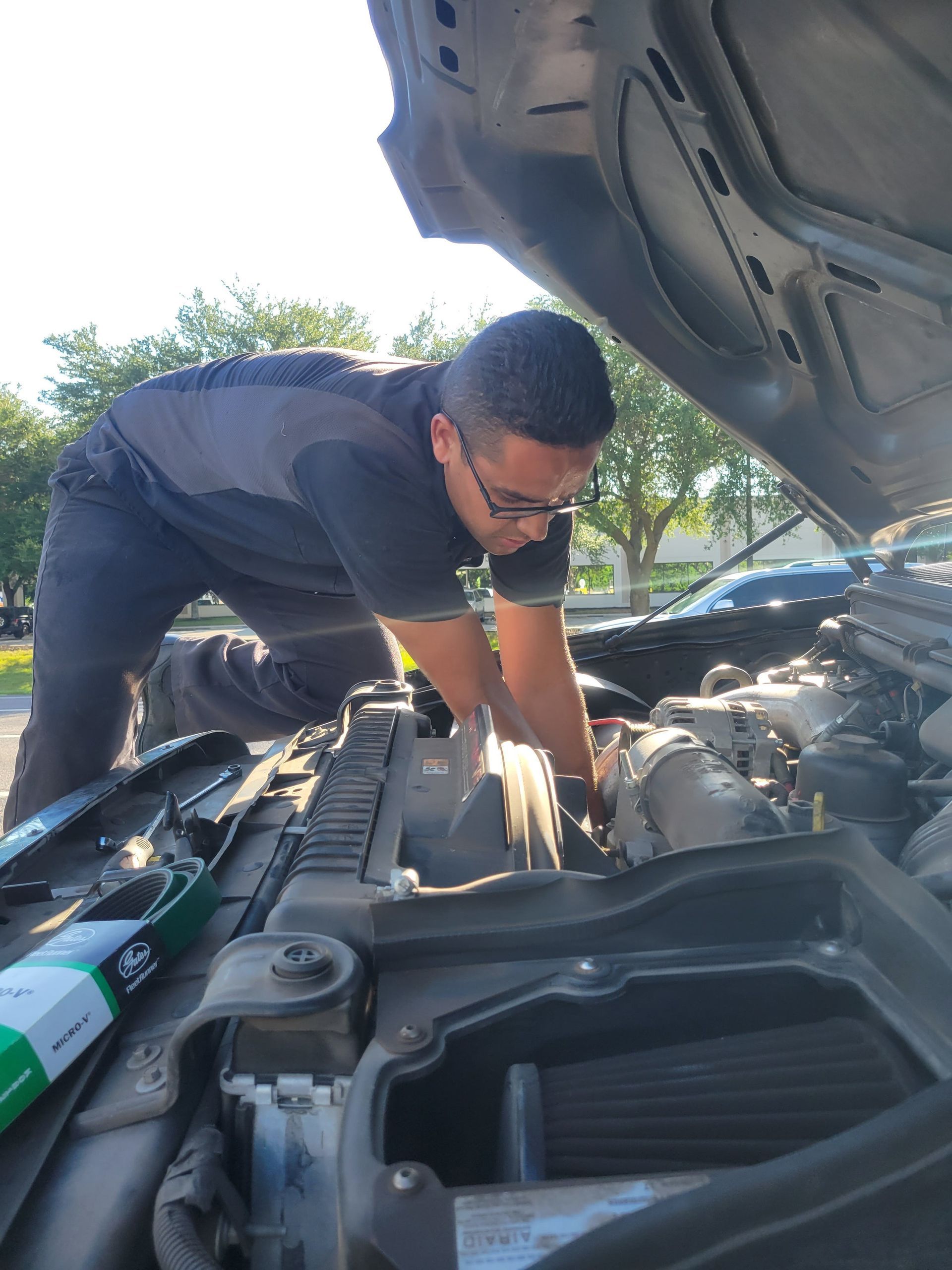 Mechanic working under the open hood of a car outdoors.