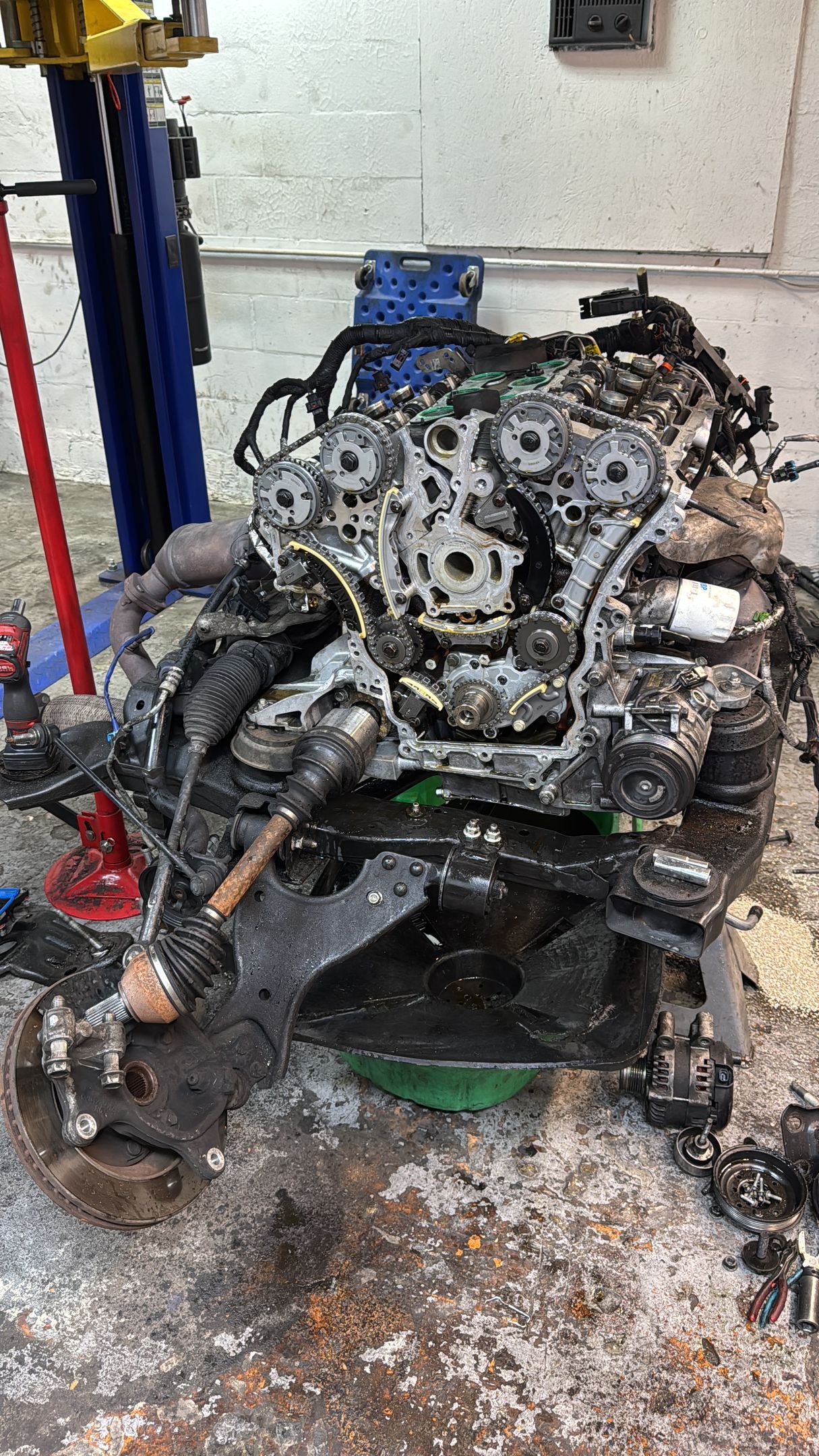 An automotive engine and drivetrain assembly, partially disassembled, resting on a stand in a workshop.