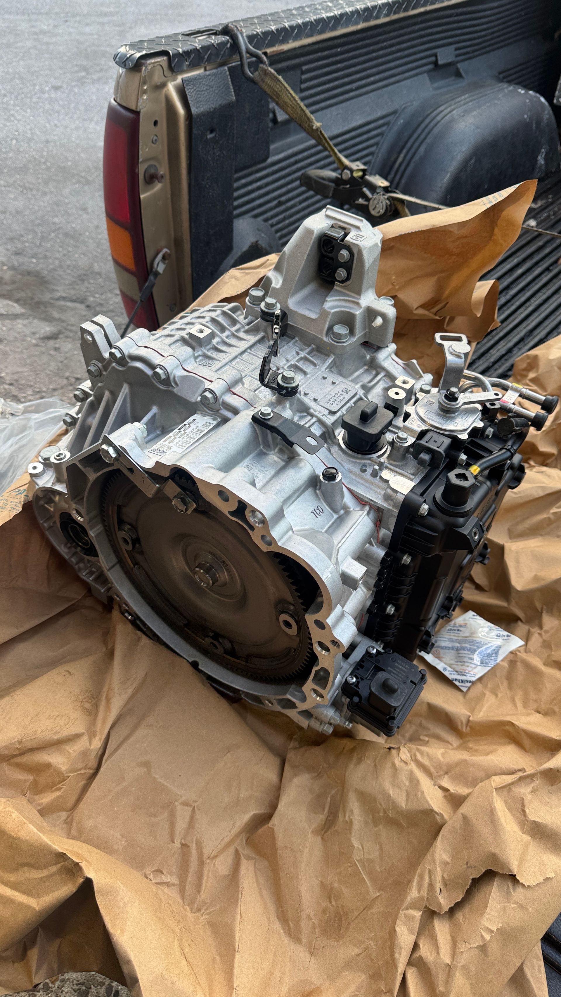 A car transmission sits on brown paper in the bed of a pickup truck.
