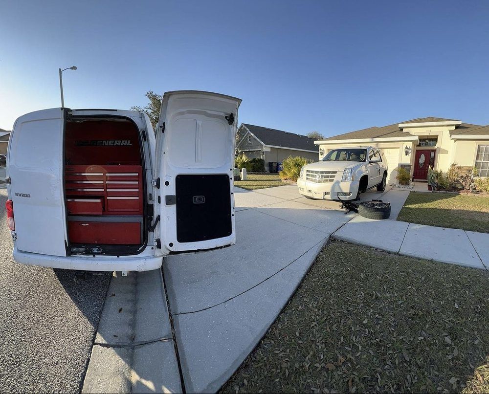White van with open back doors, red tool chest inside. SUV parked in front of house.