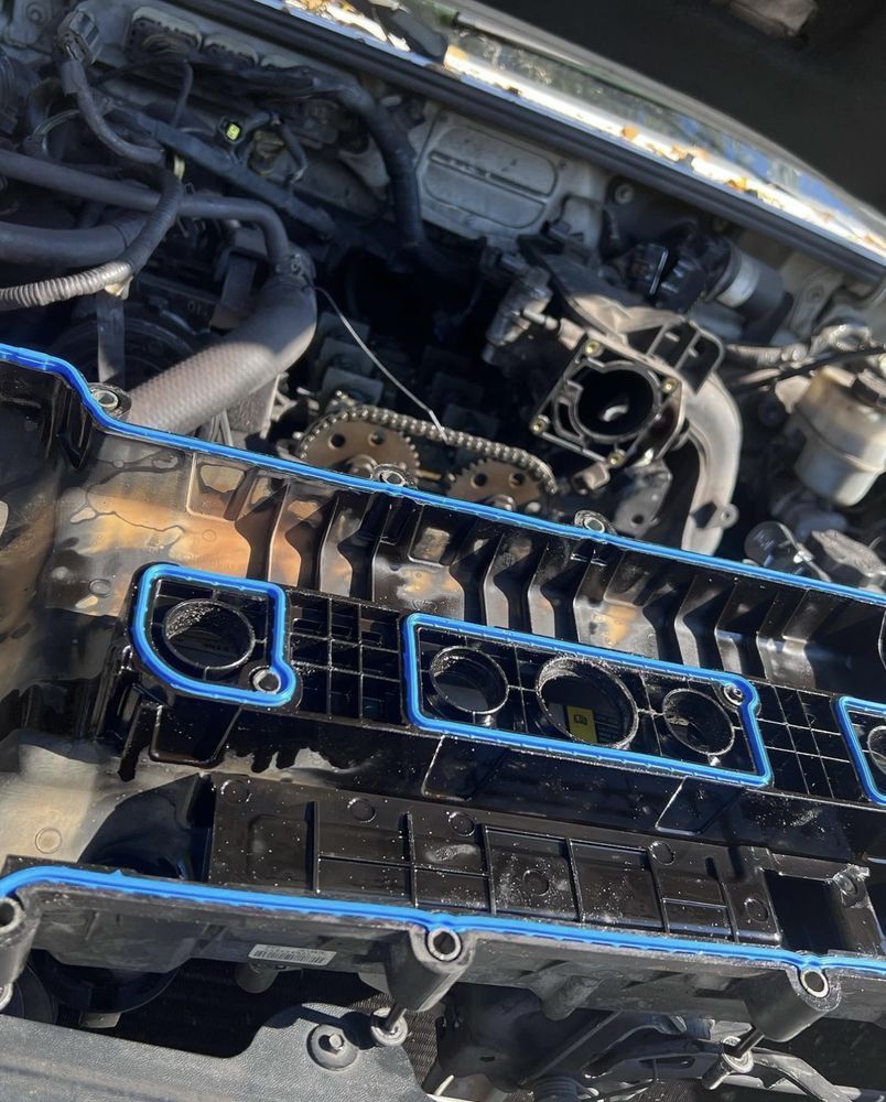 Engine valve cover with blue gasket, removed from a car engine.