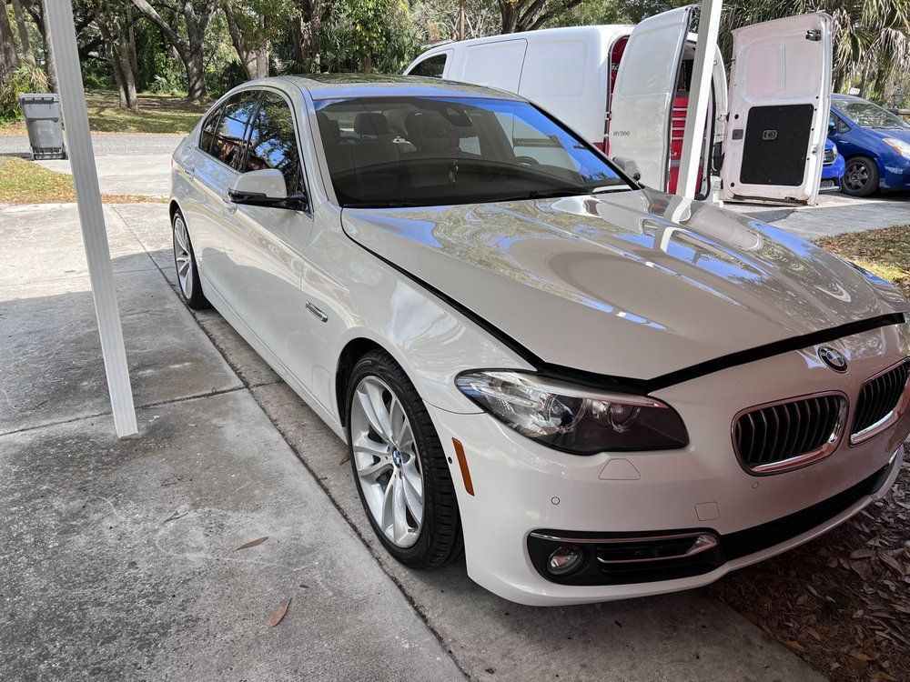 White BMW sedan parked under a carport; slight front-end damage.