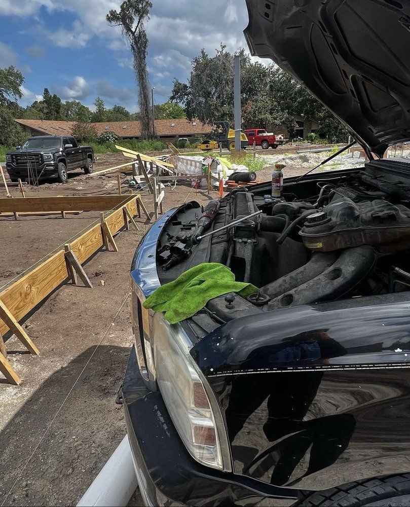 Truck with hood open, parked near a construction site. Green cloth on fender, other trucks in the background.