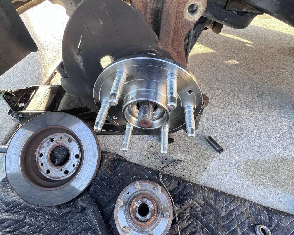 Car wheel hub assembly partially disassembled, brake rotor, and wheel bearing on a black mat.