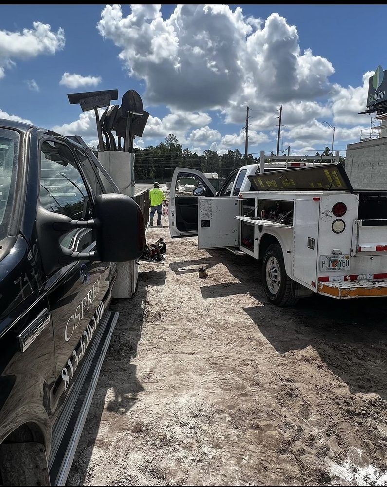 Two trucks and a worker by a concrete structure under a cloudy sky.