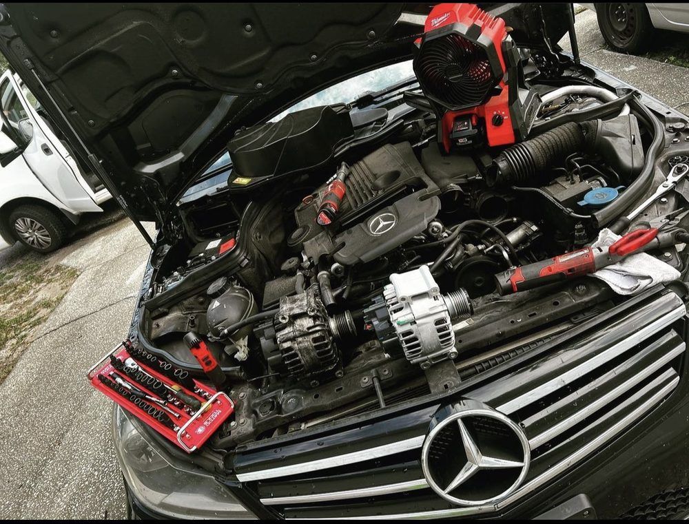 Mercedes-Benz car engine repair. Open hood, tools and a new alternator are visible.