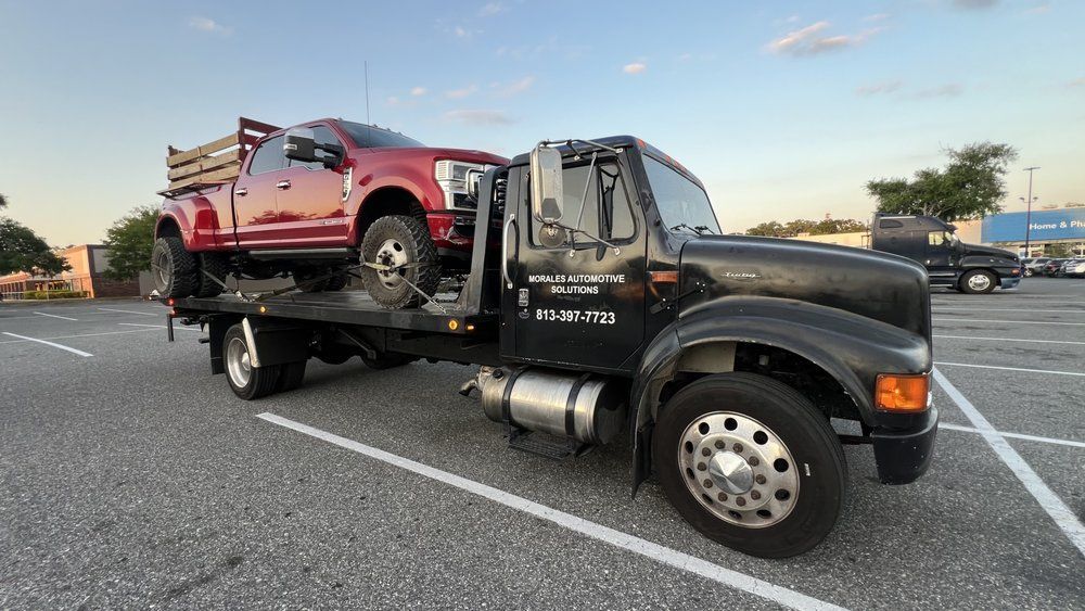 Tow truck hauling a red pickup truck in a parking lot.